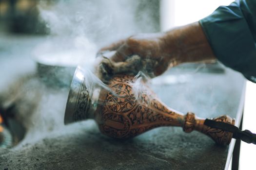 Close-up of an artisan's hand crafting a smoking decorative vase with intricate designs.