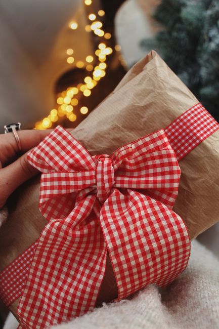 A beautiful Christmas gift wrapped in brown paper with a red checkered ribbon, held in hand.