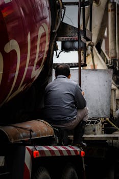 A worker in Taiwan seen from behind, sitting on construction equipment in an urban setting.