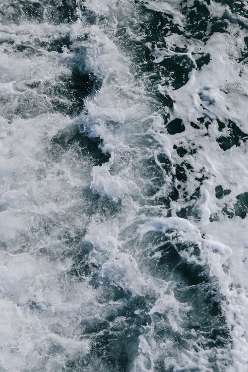 Free A vertical aerial shot capturing rough ocean waves with white foam swirling on the surface. Stock Photo