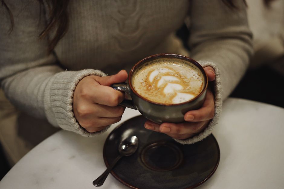 Woman holding a cappuccino with latte art in a cozy cafe setting, warm ambiance.