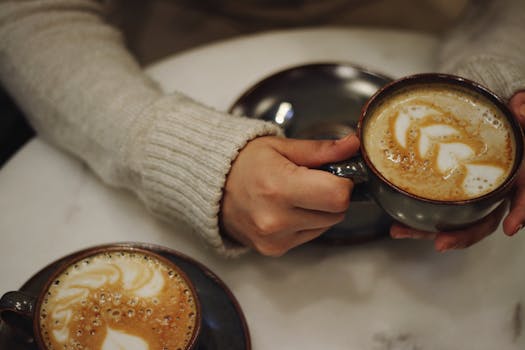 Close-up of hands holding a coffee cup with latte art in a cozy café setting.