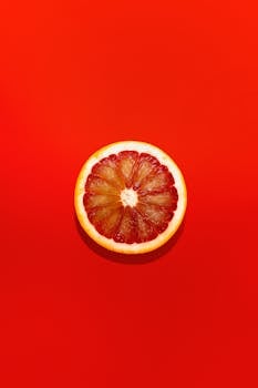 High-contrast image of a grapefruit slice centered on a vivid red backdrop.