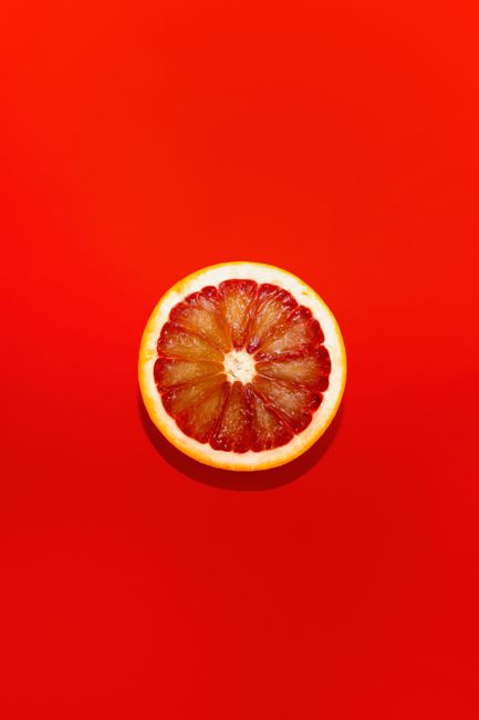 High-contrast image of a grapefruit slice centered on a vivid red backdrop.
