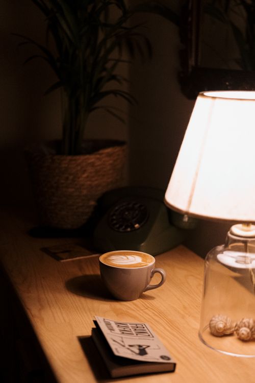 Free Warm, inviting desk setup with coffee, book, lamp, and rotary phone for a cozy ambiance. Stock Photo