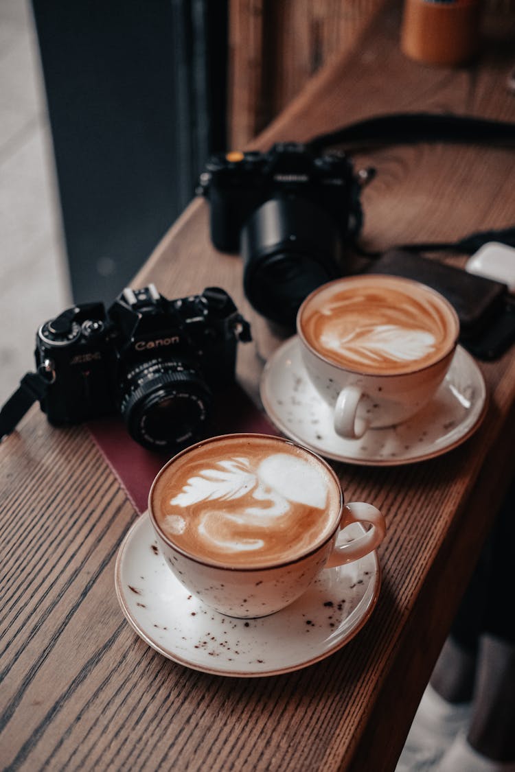 Two Cups Of Coffee And Cameras On The Table 