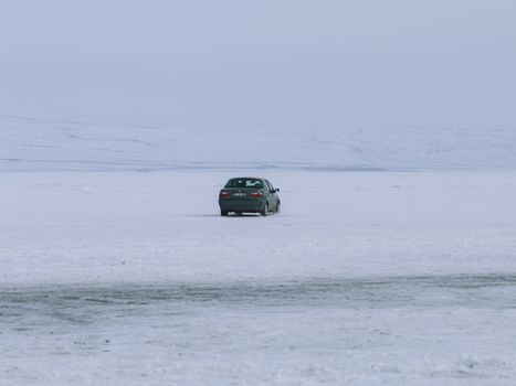 Lonely car parked on a vast, snow-covered landscape under a grey winter sky.