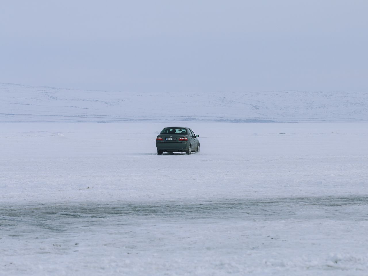 lonely car parked on a vast snow covered landscape under a grey winter