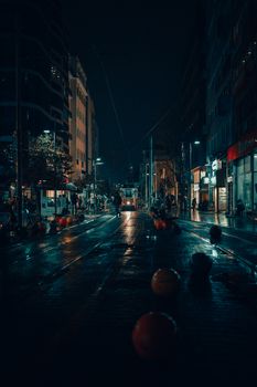 A vibrant nighttime city street featuring illuminated sidewalks, bollards, and a central tram illuminating the scene.