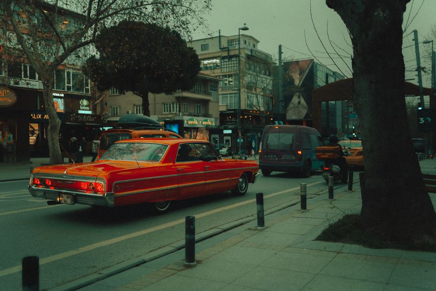 Dükkânlarla çevrili hareketli bir caddede kırmızı klasik bir araba