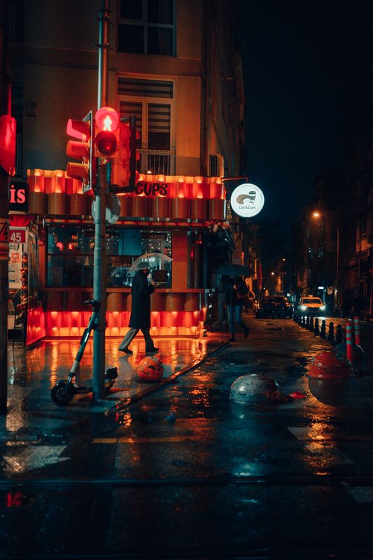 Yağmurlu bir gece sokağında neon yansımaları ve şemsiyeler