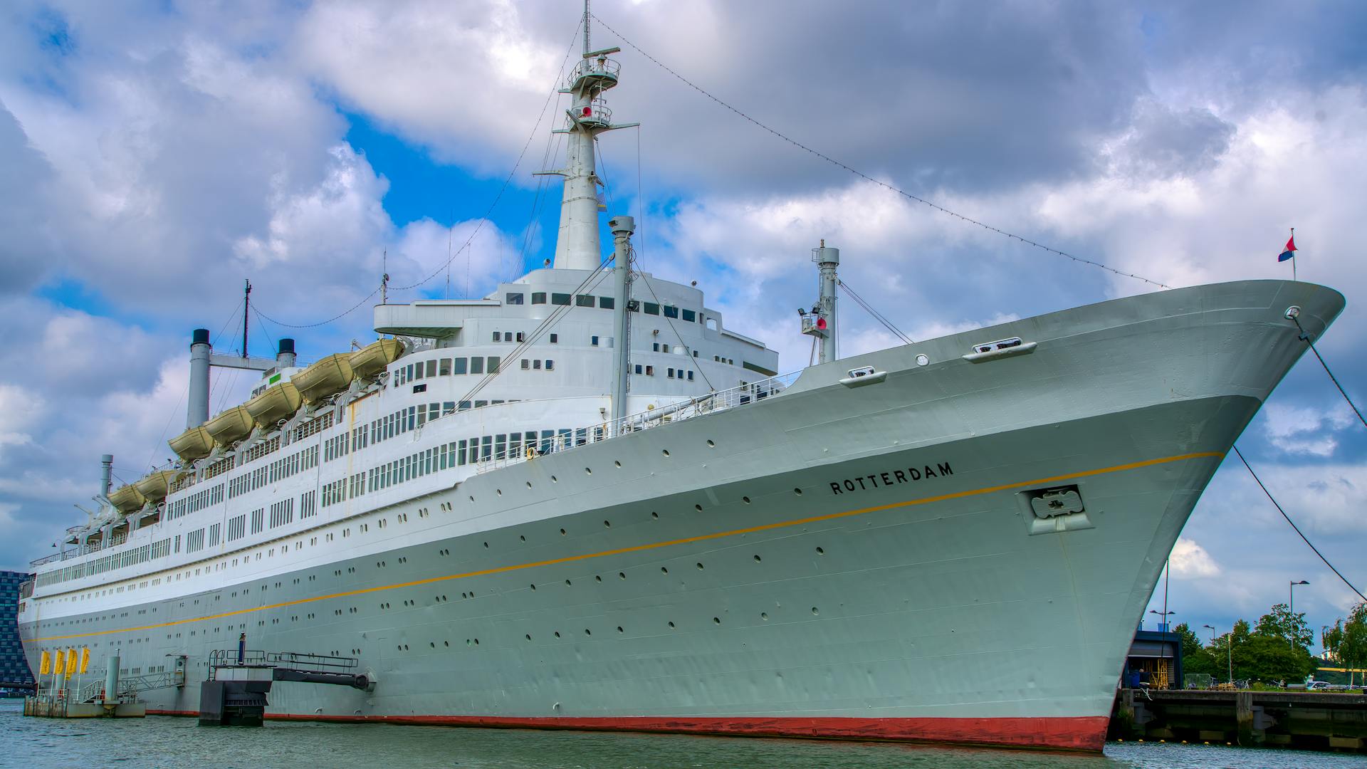 Cruise ship 'Rotterdam' moored in Rotterdam harbor under a cloudy sky.