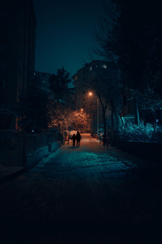 Gece ışıklı ve karlı bir sokakta siluetler