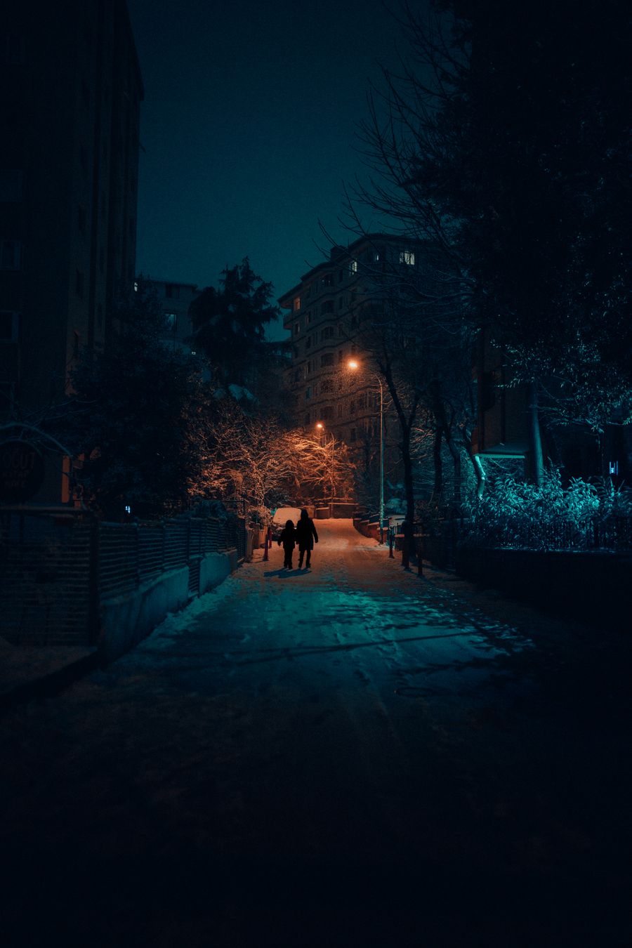 Gece ışıklı ve karlı bir sokakta siluetler