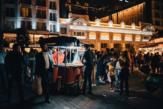 A lively night street scene with a food vendor cart surrounded by people in a busy city atmosphere.