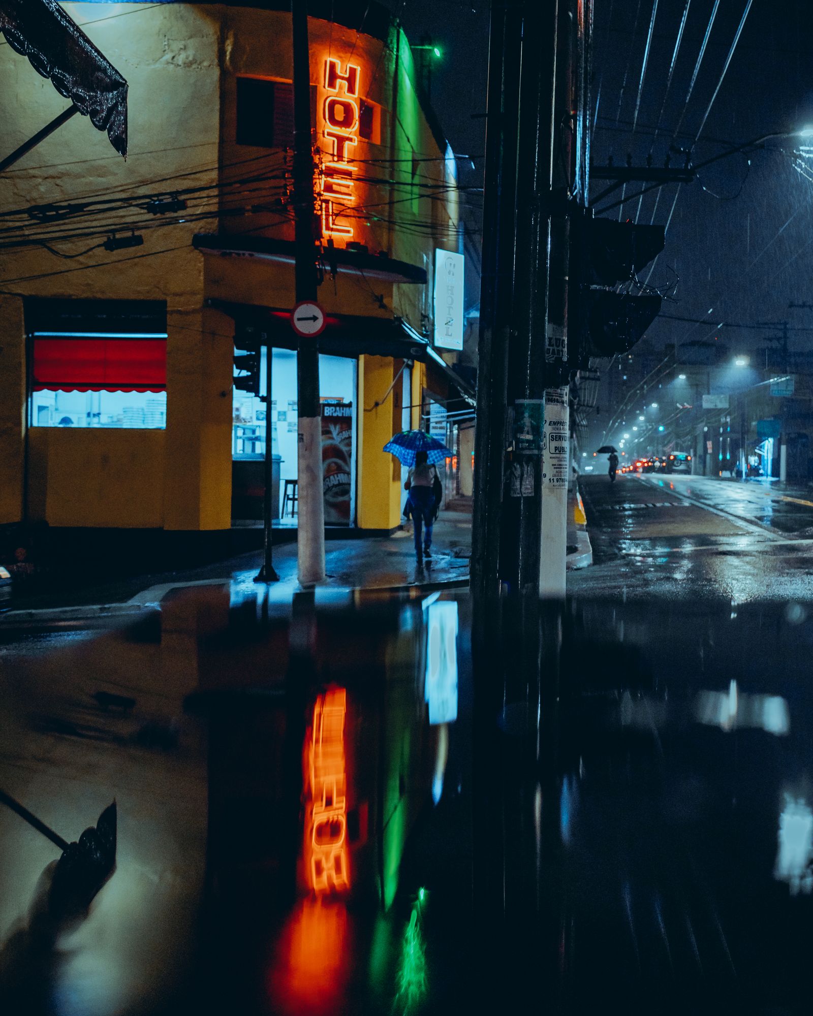 A city street at night with a neon hotel sign reflected in a rain puddle, an illustrative real photo of the rain-and-neon look the Blade Runner films made famous