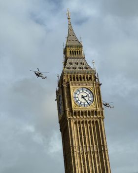 Iconic Big Ben in London with helicopters flying above, a dynamic urban landscape view.