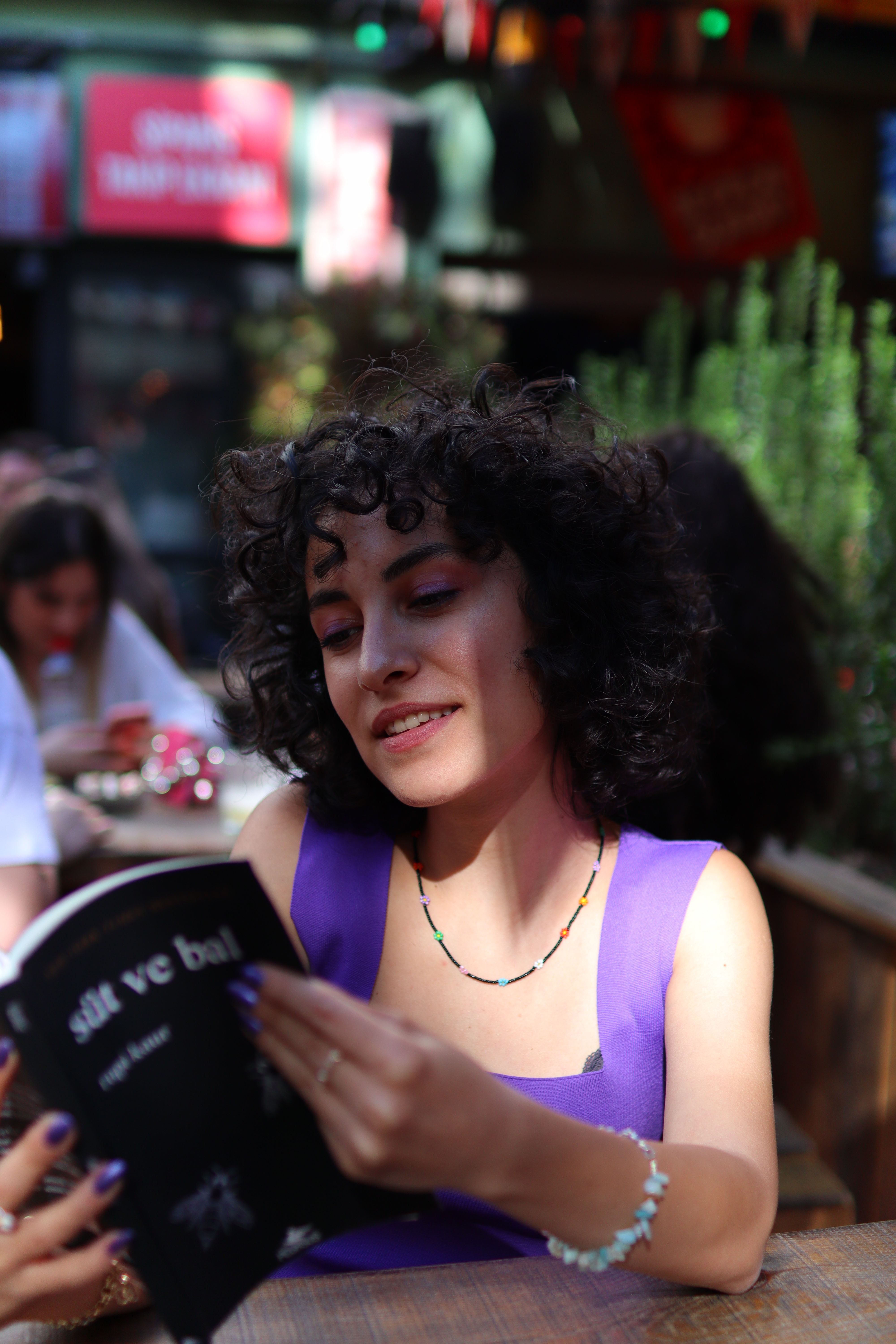 A young woman with curly hair reading a book at an outdoor café in Ankara, Türkiye.