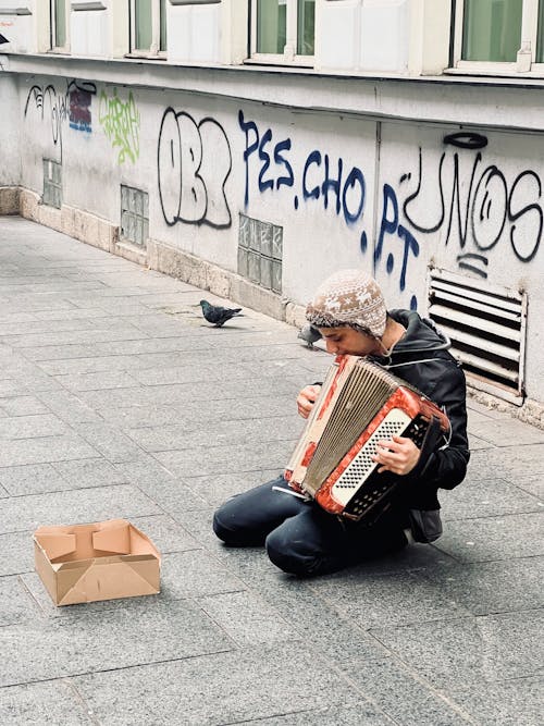 Photo of a Kneeling Man Playing the Accordion in the Street