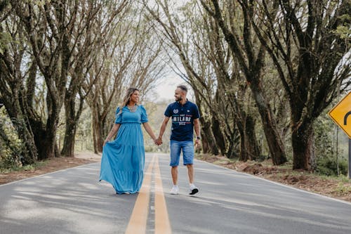 Photo of a Couple Holding Hands while Walking on a Road