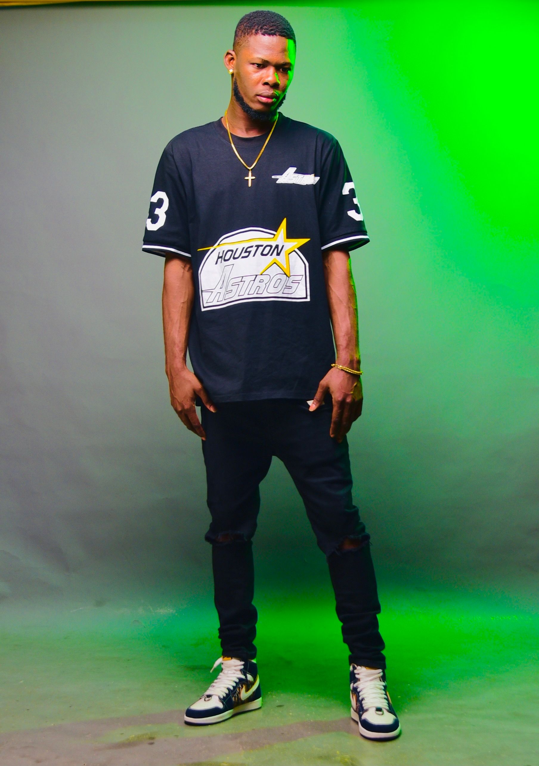 Stylish young man in sportswear standing confidently in studio with green background.