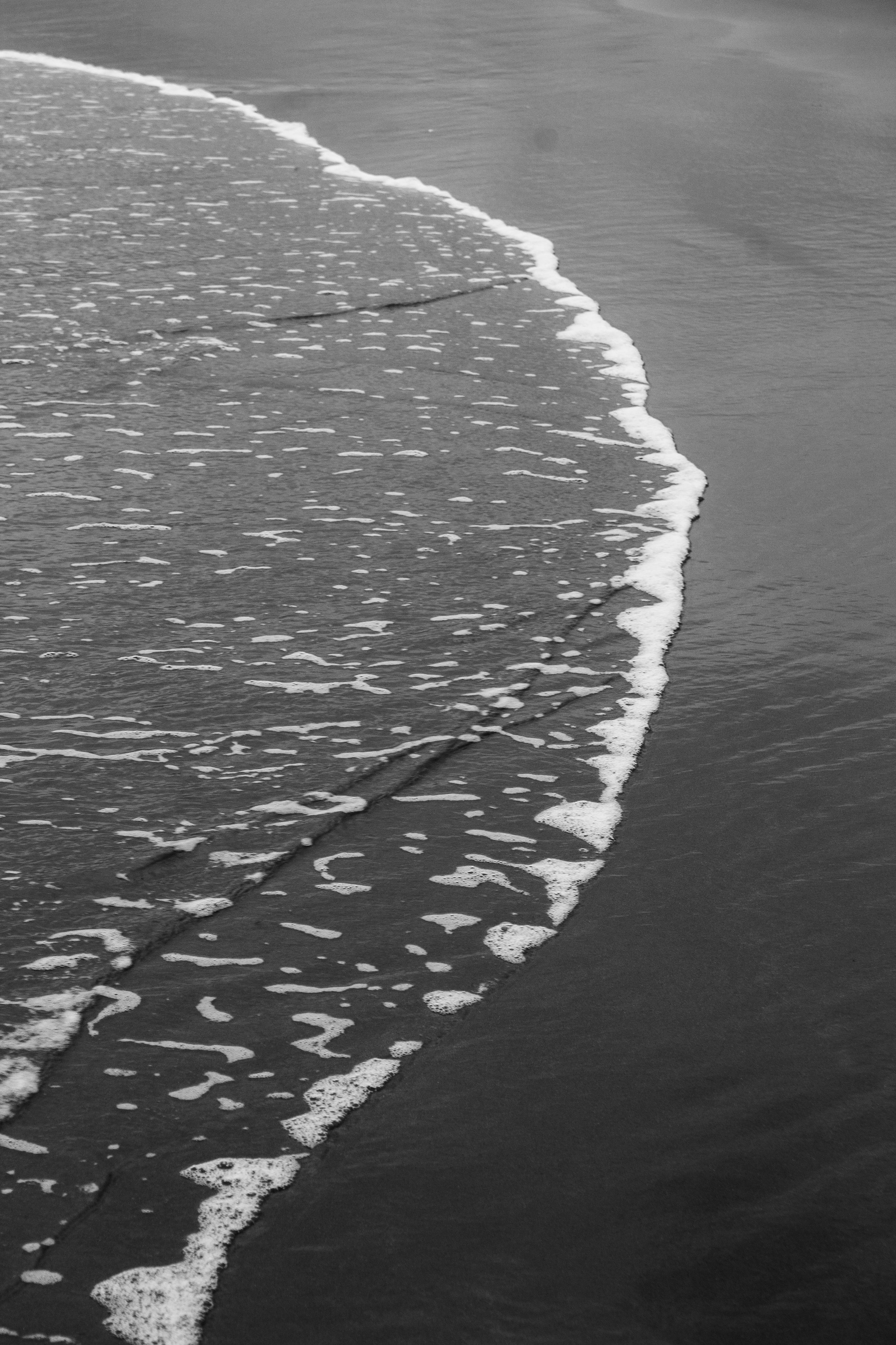 Monochrome image of ocean waves gently reaching the sandy shore, creating a serene atmosphere.