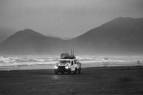 Black and White Photo of a Car Driving on the Beach
