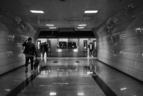 Free Monochrome image capturing people in a subway station with reflections and a departing train. Stock Photo