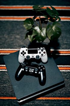A pair of gaming controllers atop a console with a monstera plant nearby, showcasing modern leisure.