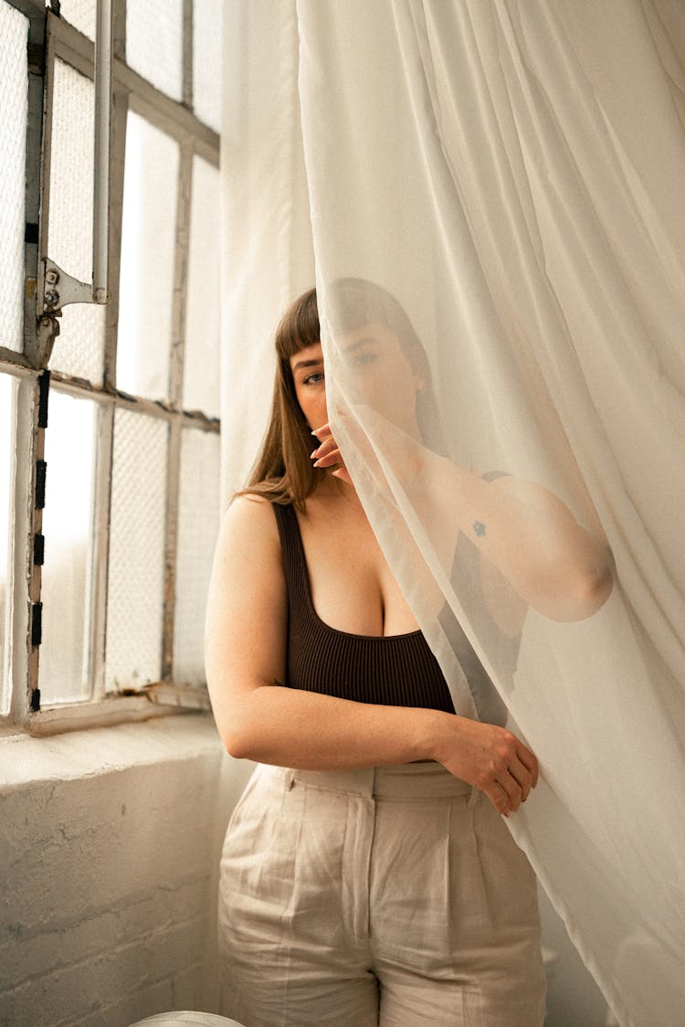 A Woman Is Leaning Against A Window With A Sheer Curtain