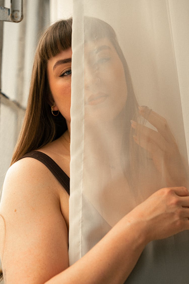 A Woman Is Looking Out Of A Window With A Curtain