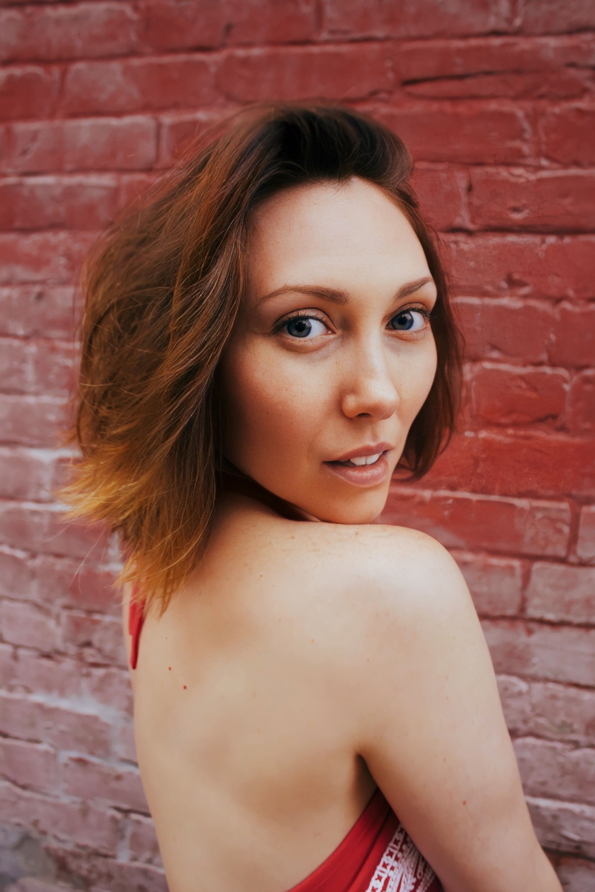Stylish portrait of a woman with a red brick wall background, showcasing elegance and fashion.