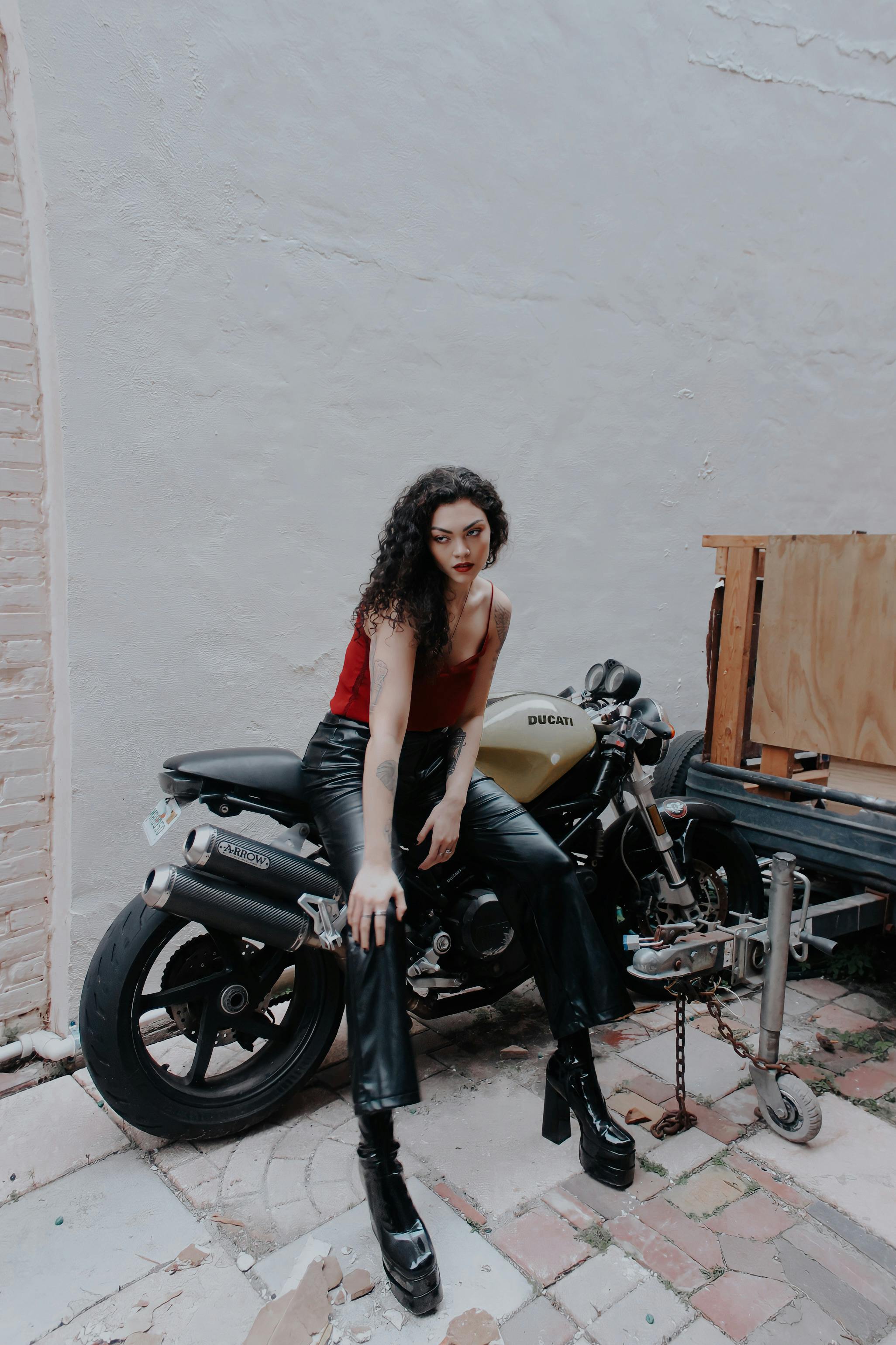 Fashionable brunette in leather poses with a Ducati motorcycle for a bold and edgy look.