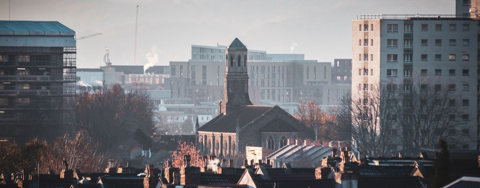 Urban view of Bristol featuring St Luke's Church amidst city buildings during a serene sunset.