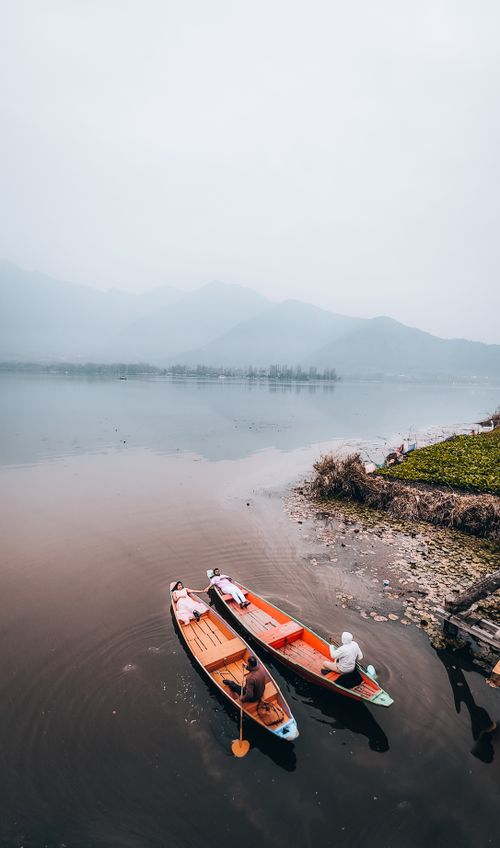 Free Two people resting in wooden boats on a calm lake surrounded by fog-shrouded hills. Stock Photo