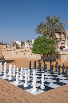 Outdoor giant chess set against a backdrop of sandy desert and palm trees at a luxurious resort.