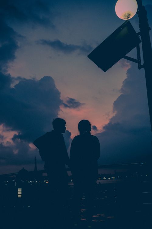 Free Silhouette of two friends enjoying a vibrant urban sunset with a pink sky. Stock Photo
