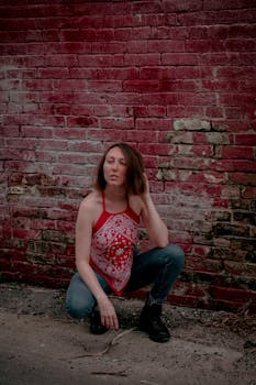Young woman wearing red bandana top and jeans against distressed brick background.