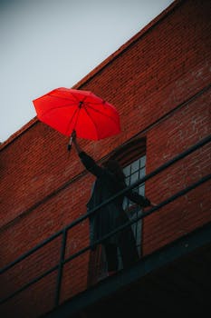 Urban scene featuring a red umbrella against a brick building. Moody and artistic vibe.
