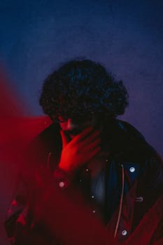 A mysterious and moody portrait of a man in deep thought under red and blue lighting.