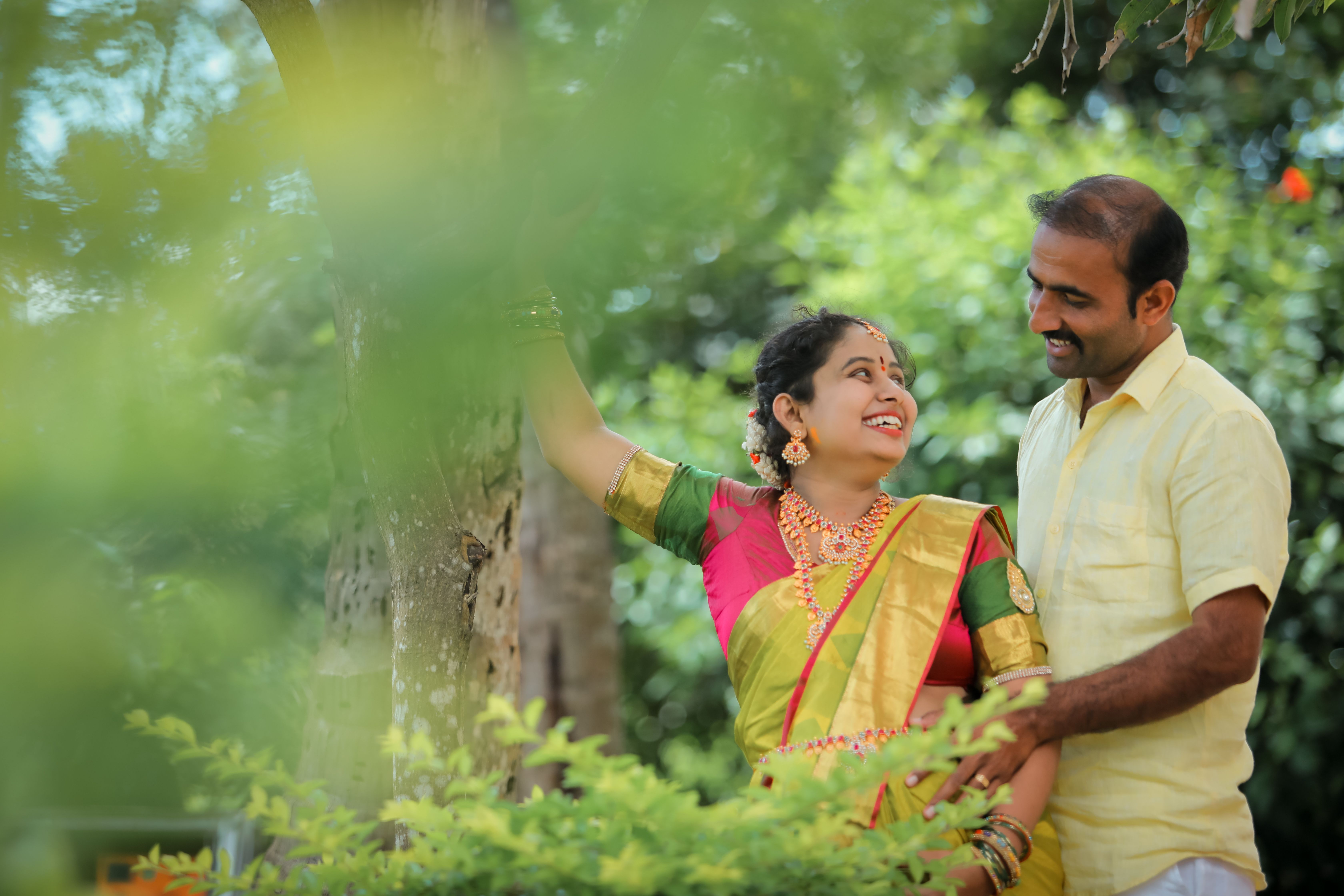 Joyful South Asian couple in traditional attire enjoying a romantic moment outdoors surrounded by nature.