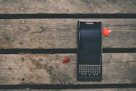 一张乡村木桌上放着一部黑莓智能手机，周围散落着红色花瓣，拍摄于户外