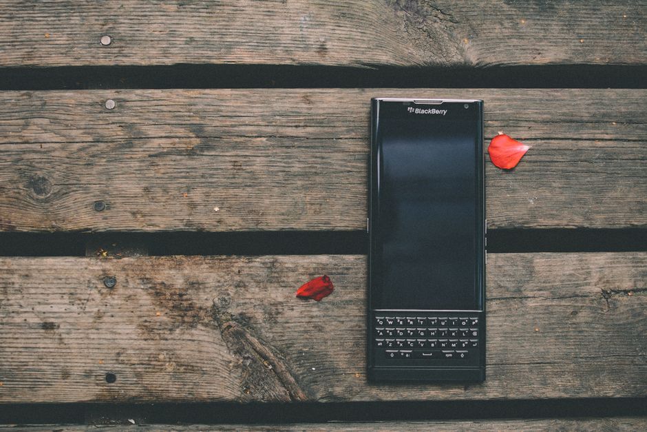 A BlackBerry smartphone on a rustic wooden table with red petals scattered around, captured outdoors.