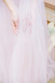 Delicate close-up of a woman's hands holding a soft chiffon bridal veil in gentle pastel hues.