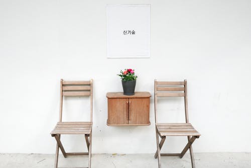 Photo of Two Wooden Chairs and a Wooden Cabinet Against a White Wall