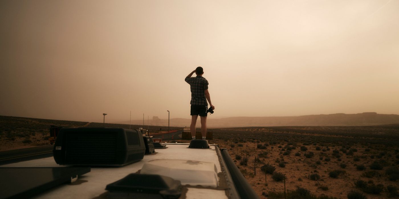 A person standing on an RV roof beside its vents and air conditioner