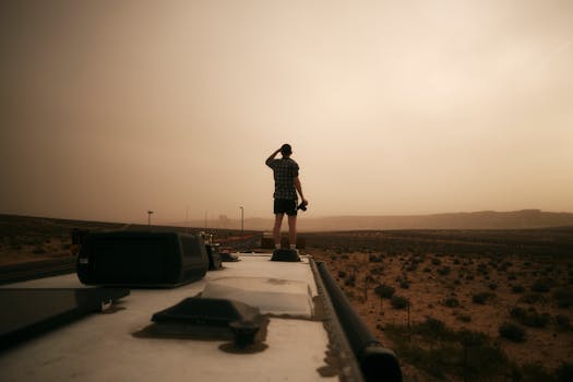 Traveler standing on an RV roof, gazing at the Arizona desert during evening light, evokes a sense of adventure.