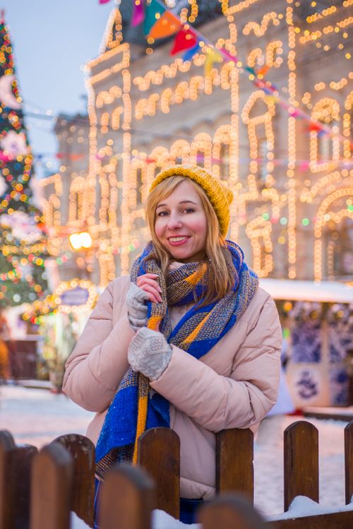 Free Smiling woman in winter clothing enjoying festive lights on a snowy day. Stock Photo