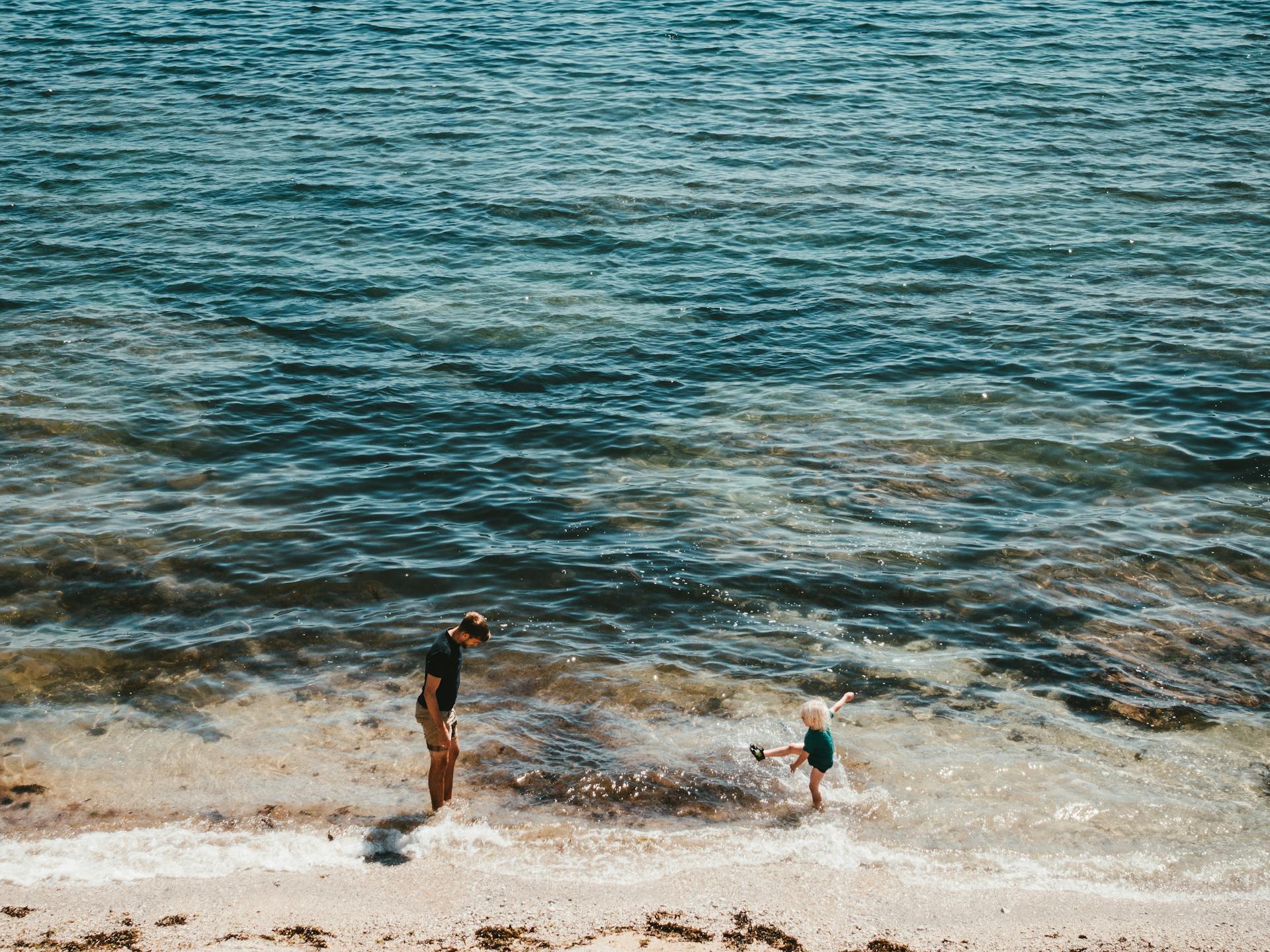A joyful moment of a father and child playing by the sea on a sunny day at Falmouth beach.