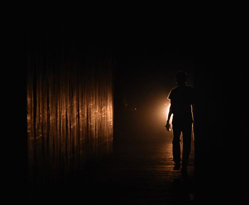 Free Silhouette of a person walking in a dark hallway illuminated by warm light. Stock Photo